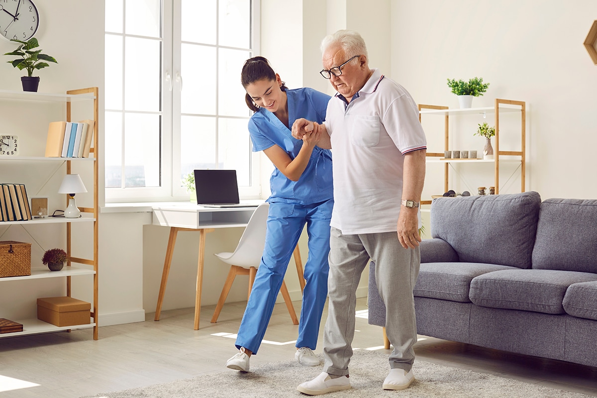 Nurse in assisted living facility holding patient by hand and helping him walk